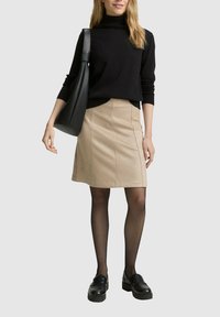 Maglione a collo alto nero, gonna a matita in suede beige con cuciture verticali, collant neri e scarpe slip-on nere chunky; borsa a spalla in pelle nera.
