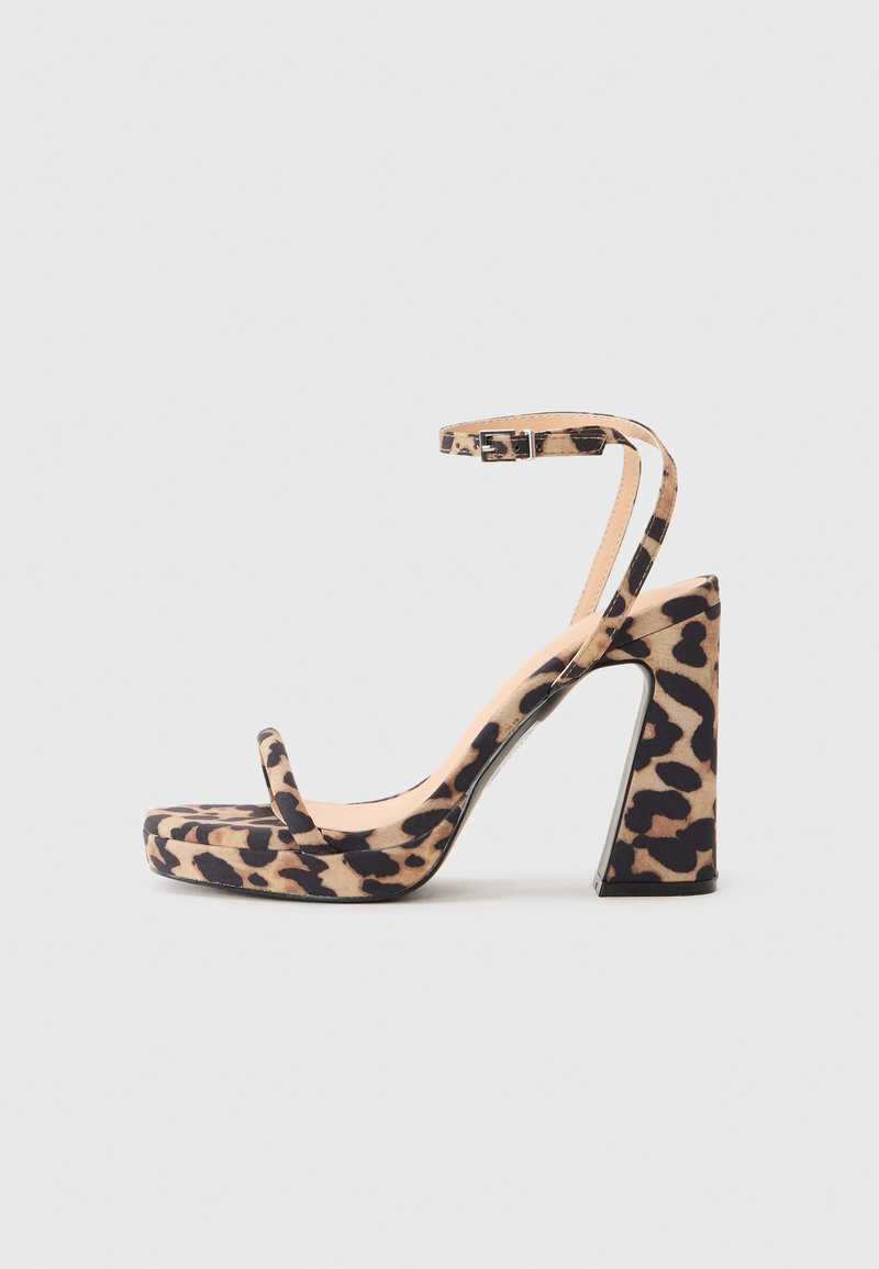 Pumps i leopardmønster med høy hæl, tykk blokkhel, ankelstroppe og en jevn tekstur overflate. Har en plattformtådesign.