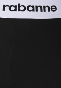 Svarta elastiska leggings med en vit midja som har "rabanne"-logotypen i svart. Tyget ser slätt ut med en jämn textur.