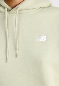 Sweatshirt verde-claro com um tecido texturizado, cordões ajustáveis e um logótipo branco bordado no peito.