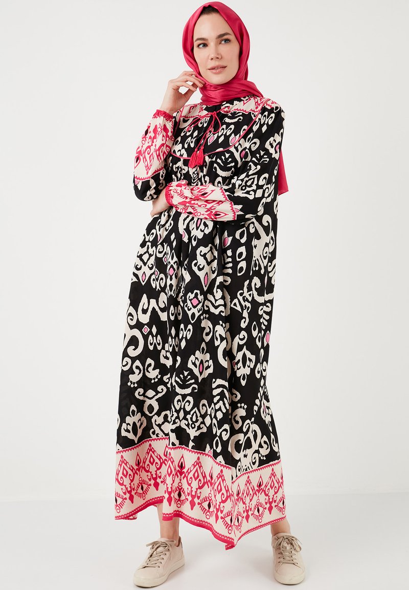Black dress with white and pink abstract patterns, long sleeves, pink accent details, and tassel. Paired with light-colored sneakers.