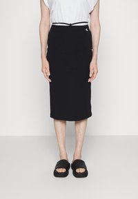 Svart midikjol i mjukt tyg med figurnära design och elastisk midja. Bärs med en enkel vit t-shirt och svarta sandaler.