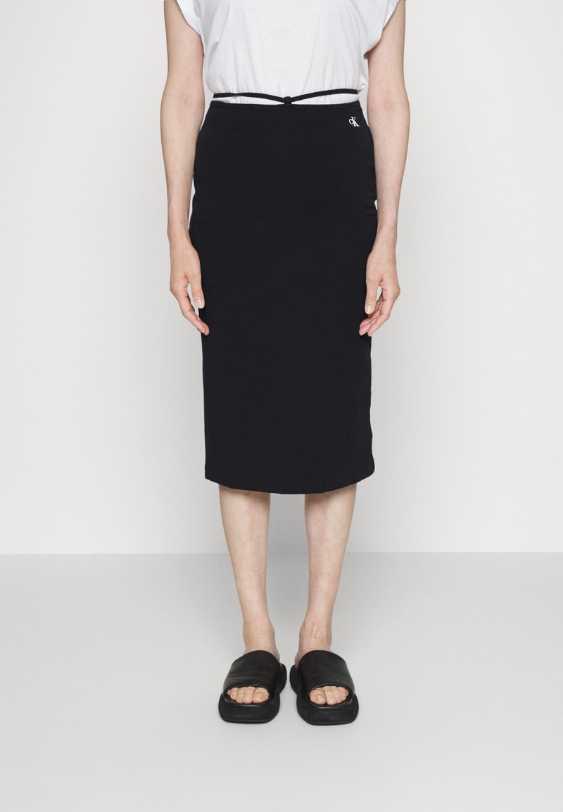 Svart midikjol i mjukt tyg med figurnära design och elastisk midja. Bärs med en enkel vit t-shirt och svarta sandaler.