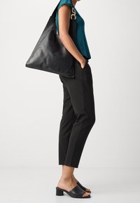 Person som bär en teal-färgad topp, svarta smala byxor, svarta klackslip-insandaler och bär en stor svart läderaxelväska.