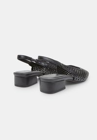 Zapatos slingback perforados negros con punta cerrada, tacón grueso y textura lisa. Incluyen una correa para el tobillo que brinda soporte.