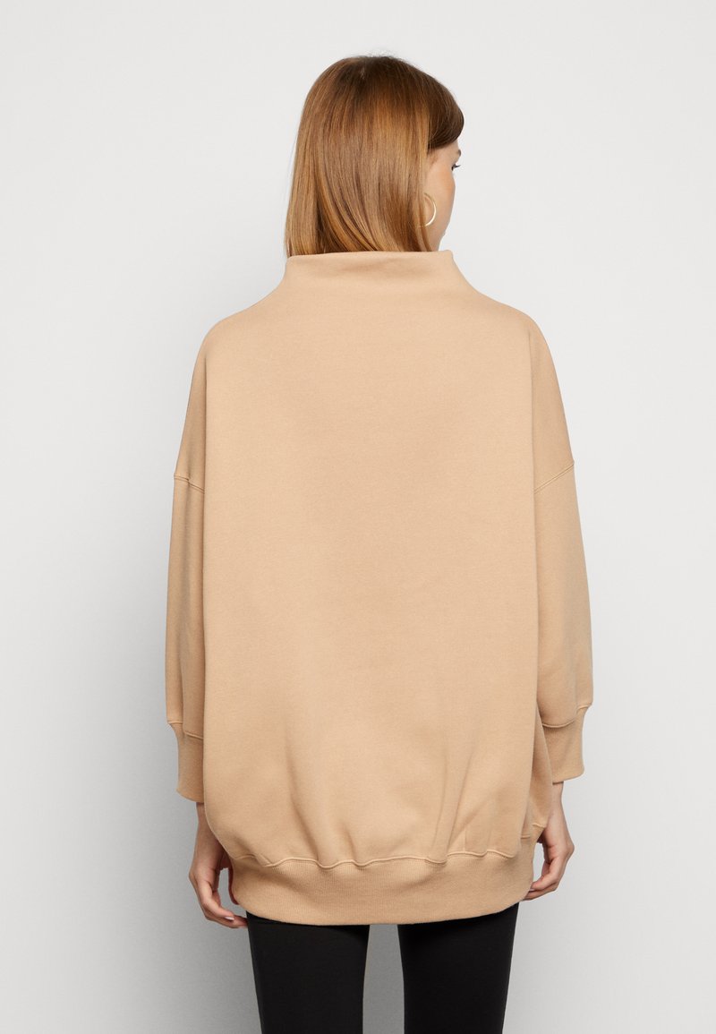 Felpa over-size beige con collo alto, spalle scese e orlo a coste. Tessuto morbido, senza motivi visibili o hardware.