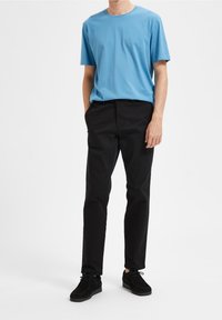 Blå bomullströja med rundad halsringning, i kombination med svarta stretchbyxor och svarta mockaskor. Enkel, rak skärning.