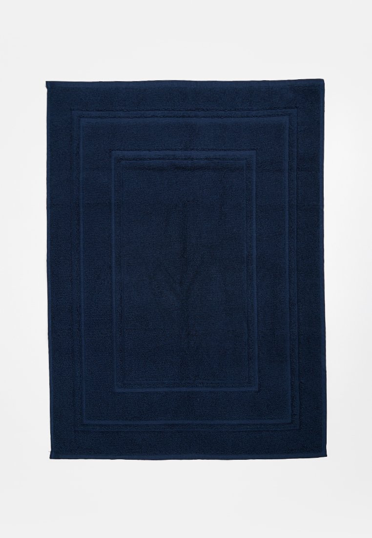 Tapis de bain rectangulaire bleu foncé avec un motif de bord texturé sur un fond blanc uni.
