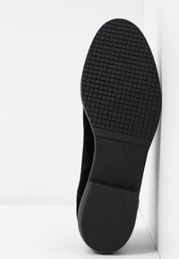 Semelle de chaussure en suède noir avec caoutchouc texturé, présentant un motif en grille pour une meilleure adhérence. Taille 37 indiquée sur le côté.