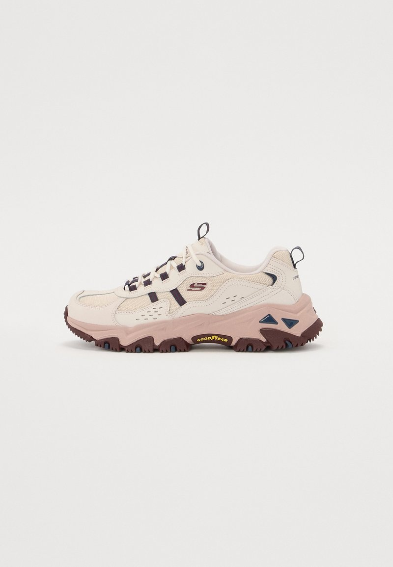 Baskets Skechers beige et marron avec lacets noirs, semelle robuste arborant la marque Goodyear, et languettes de tirage sur la languette et le talon.