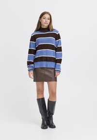 Maglione a righe in blu, marrone e bianco, con un collo alto. Abbinato a una mini gonna in pelle marrone e stivali neri fino al ginocchio.