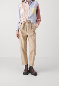 Gestreepte shirt in pastelkleuren met een gele pocket, gecombineerd met beige hoog-wijze broek en bruine chunky-sole laarzen.