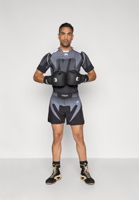 Fekete és szürke sportos öltözék, testre szabott rövid ujjú pólóval és rövidnadrággal, fekete bokszkesztyűkkel, valamint fekete és barna lábbelivel.