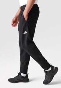 Czarne spodnie sportowe o tapered fit, elastycznym pasie i zapinanych na zamek bocznych kieszeniach. Posiadają białe logo na lewej udzie.