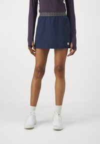 Námořnická sportovní sukně s elastickým pasem a vzorovaným lemem, v kombinaci s bílými sportovními botami a ponožkami do poloviny lýtek.