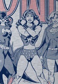Camiseta gris con ilustraciones al estilo cómic de tres superheroínas: Batgirl, Wonder Woman con un traje de patrón estelar y Supergirl.