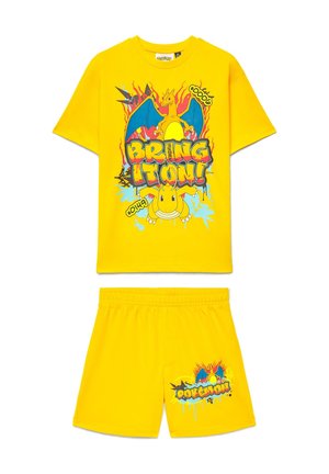 Completo giallo due pezzi con grafiche di Charizard e Dragonite, scritta "Bring it on!" sulla maglietta e logo Pokémon sui pantaloncini.