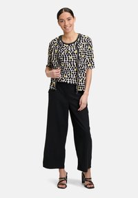 Czarne spodnie o szerokich nogawkach w zestawieniu z bluzką z krótkim rękawem w zwierzęcy wzór z żółtymi akcentami oraz kardiganem zapinanym na zamek. Gładka tekstura, lekki materiał.
