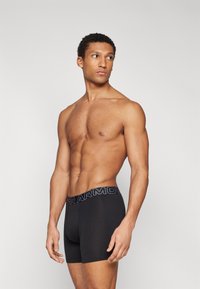 Fekete boxer alsónadrág kontrasztos derékkal, amelyen vastag betűkkel szerepel az "UNDER ARMOUR" felirat. Simább anyag és testhezálló fazon.