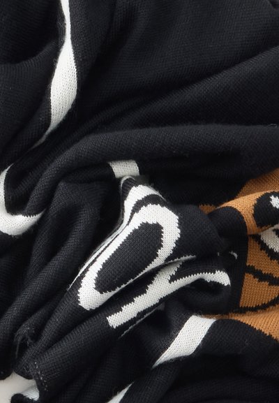 Tissu noir avec des motifs graphiques blancs et marron, plié et froissé, montrant une texture de tricot et des éléments de design contrastés.