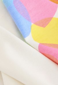 Tessuto di cotone con grandi motivi geometrici colorati in rosa, blu e giallo, sovrapposti a un tessuto bianco e morbido.