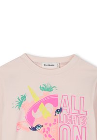 Ανοιχτό ροζ μπλουζάκι με γραφικό σχέδιο μιας καμηλοπάρδαλης με κέρατο μονόκερου, ζωντανά χρώματα και το κείμενο "ALL LIGHTS ON" με έντονα γράμματα.