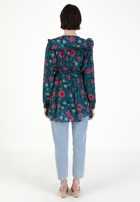 Top w kolorze teal w kwiatowy wzór z falbanym dekoltem, z paskiem w talii i długimi rękawami, zestawiony z jasnoniebieskimi dżinsami i beżowymi sandałami na słupku.