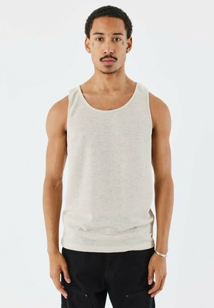 Beige tanktop gemaakt van textuurstof. Heeft een ronde halslijn en brede armsgaten, gecombineerd met zwarte cargobroek. Minimalistisch ontwerp.