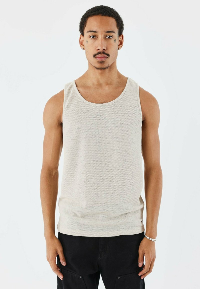 Débardeur beige en tissu texturé. Doté d'un col rond et de larges emmanchures, associé à un pantalon cargo noir. Design minimaliste.