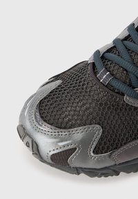 Black athletic shoe featuring a mesh upper, silver textured accents, and dark teal laces, with a reinforced toe and rubber outsole.