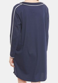 Persona che indossa un vestito lungo e largo di colore blu navy con profili bianchi lungo le spalle e i bordi delle maniche, visto di spalle.