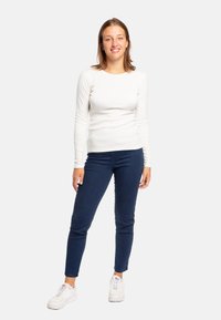 Camicia bianca a maniche lunghe abbinata a jeans fitted blu scuro e sneakers bianche. L'outfit presenta un design semplice e pulito, senza motivi visibili.