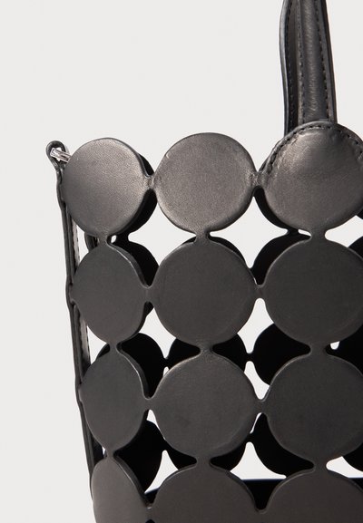 Sac en cuir noir avec des découpes circulaires, au design structuré et à la texture lisse. Une bandoulière réglable est attachée.