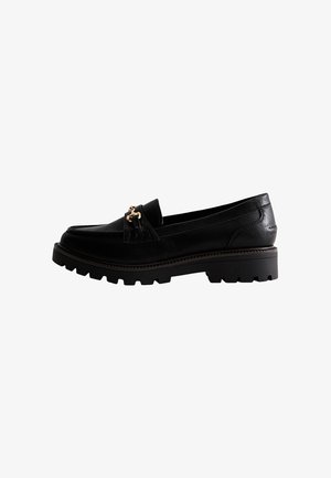Mocassin en cuir noir avec semelle en caoutchouc épaisse et détail mors doré sur le dessus, vue latérale sur fond blanc.