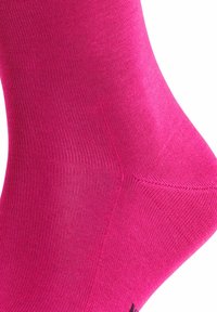 Calzino rosa con una consistenza liscia e un design a costine. Le aree delle dita e del tallone sono rinforzate e presenta un logo scuro vicino alla caviglia.
