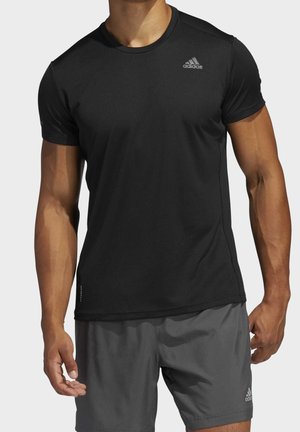 Homme portant un t-shirt de sport Adidas noir à manches courtes et un short Adidas gris foncé, debout, les bras détendus le long du corps.