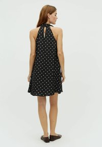 Rochie neagră făr�ă mâneci, cu buline albe, design cu gât halter, spate cu deschidere tip cheie, siluetă fluidă și margine solidă.