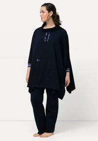 Tummansininen poncho, jossa on kauluksen näköinen kaulus, etutasku ja raidalliset yksityiskohdat hihoissa, yhdistettynä sopiviin tummansinisiin housuihin. Pehmeä kangas.