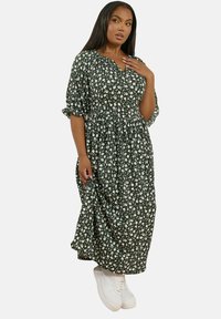 Blommig grön maxiklänning med puffärmar, rynkad midja och vita blommönster, matchad med vita sneakers.