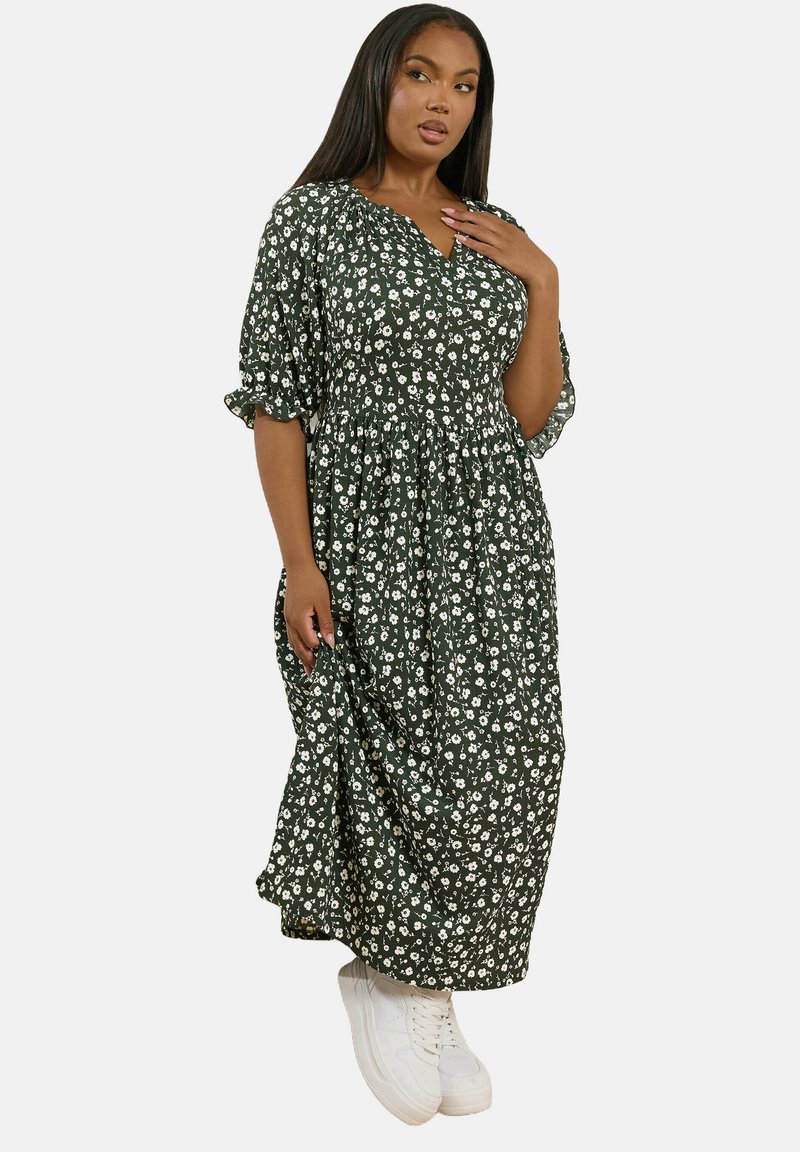 Blommig grön maxiklänning med puffärmar, rynkad midja och vita blommönster, matchad med vita sneakers.