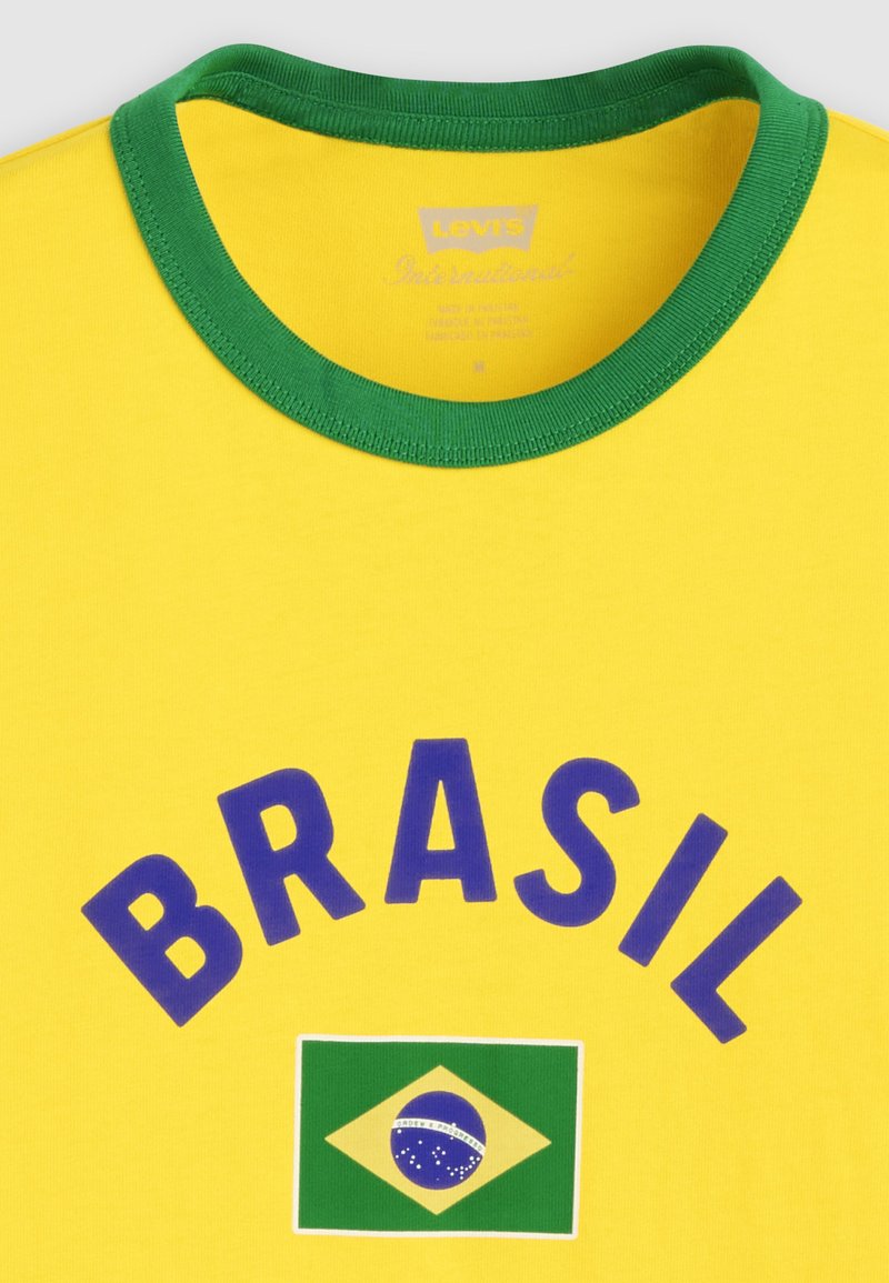 T-shirt jaune avec col vert, "BRASIL" en lettres bleues, et un petit drapeau brésilien centré sous le texte.