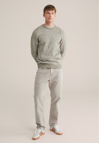 Maglione a maglia grigio chiaro con scollatura e polsini a coste, abbinato a pantaloni beige chiaro e sneakers bianche con dettagli marroni.