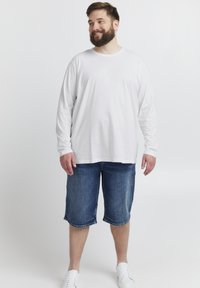 Weißes langärmliges T-Shirt, blaue Denim-Shorts und weiße Sneakers. Das Outfit hat eine lockere Passform und ein einfaches Design ohne Muster.