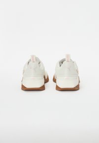 Sneaker bianchi e grigie con tomaia in rete testurizzata, dettagli rosa chiaro e suola in gomma marrone. Presentano un occhiello per il piede e un dettaglio del logo sul tallone.