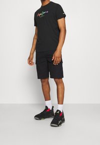 T-shirt en coton noir avec un logo "Pepe Jeans London" multicolore, associé à un short cargo noir et des baskets noires avec des accents rouges.