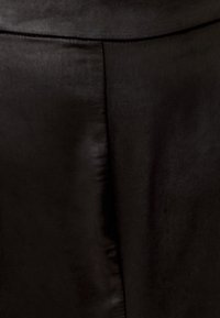 Tessuto nero con una trama liscia e una leggera lucentezza. Presenta una cucitura che corre verticalmente, mostrando un design semplice e minimalista.