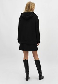 Svart oversized hoodie i mjukt material, med en känguruficka och dragsko på huvan, parat med en svart minikjol och knähöga stövlar.