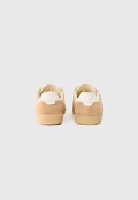 Beige semskinnsneakers med en kremfarget hæl, rund form, gummisåle og stitchingdetaljer langs sømmene. Sett fra bak.