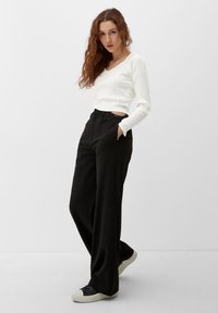 Witte geribbelde long-sleeve top met V-hals, gecombineerd met hoge zwarte broeken en zwarte sneakers. Opvallende zijzakken op de broeken.