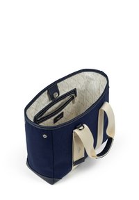 Marinblå canvasväska med krämfärgade handtag, som har ett rymligt inre, en dragkedjeficka och mönstrad foder. Detaljer inkluderar silverfärgade metalldelar.